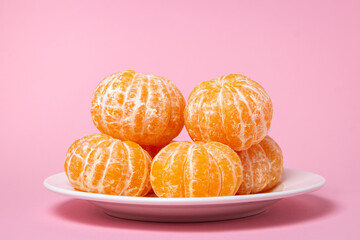 Peeled tangerines on a plate on a pink background. Citrus fruit on colored background