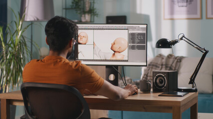 Back view of anonymous man creating 3D model of videogame character while sitting at table and...