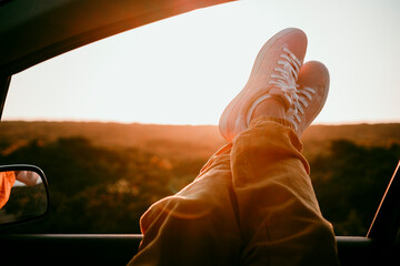 Woman relaxing with crossed legs on car window while enjoying golden hour