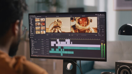 Back view of male content creator using computer to edit cosmonaut video during remote work from home