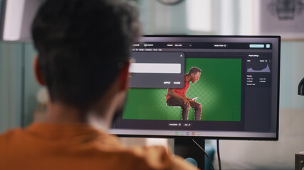 Back view of anonymous man integrating 3D graphic into video with real person while sitting at table and using computer in home office