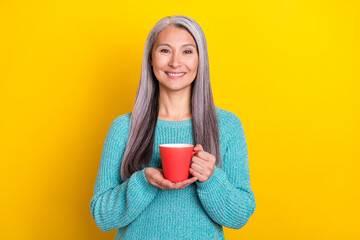 Portrait of attractive cheerful grey-haired woman holding in hand drinking herbal tea isolated over bright yellow color background