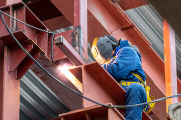 A welder with a protective mask for welding metal and sparks performs welding work on a...