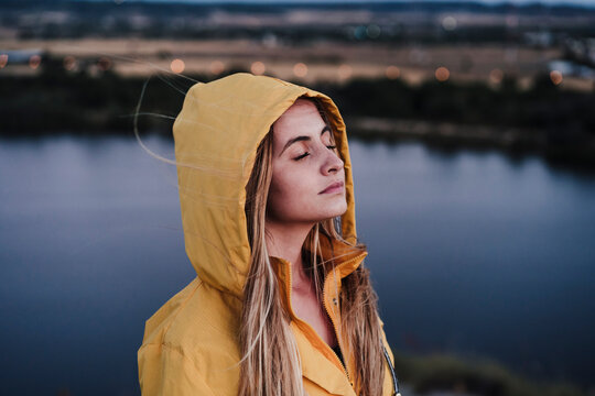 Young woman with eyes closed wearing yellow raincoat at sunset