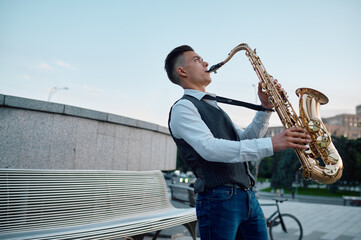 Saxophonist plays melody at the bench in city park
