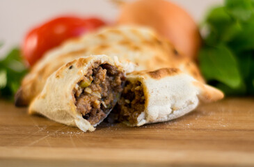 empanada cortada a la mitad rellena de carne con ingredientes alrededor