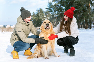 Portrait of young family with..Golden retriever in winter outdoors in forest.