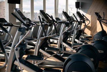 Interior of the modern gym with large windows. Elliptical trainers orbiter and treadmills.