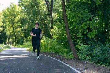 Young woman with weight excess runs in the park. Girl with curvy figure goes in for sports to lose extra pounds.