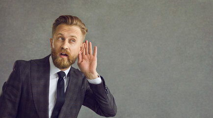 Businessman with hand cupped to ear. Man showing deafness listening gesture sign. Adult entrepreneur in business suit hearing to rumor or gossip. Headshot portrait with copy space aside