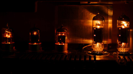 Close up silhouette of eletronic vacuum radio tube. Old analog electronic audio components glowing orange.