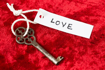 Vintage key with label attached bearing the word Love on red velvet background