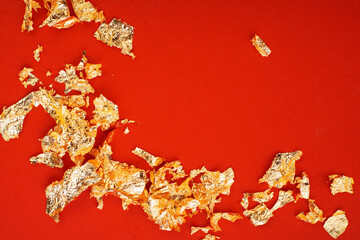 Sheets of gold foil flakes on a luxurious festive red background. Luxury