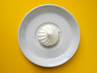 Top view of a meringue on a round white plate on a yellow background.