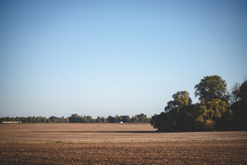 plowed agricultural field forest and green meadow in distance