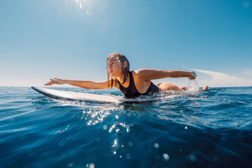 Surf girl rowing on surfboard. Attractive surfer woman in sea and sunny day