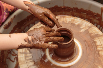 The child moulds from clay a pot on a potter's wheel. Adults help the child to work with clay.