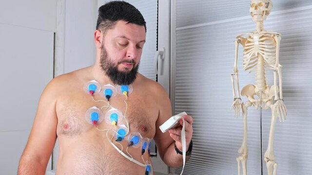 A man wearing portable holter monitor device connected to chest, setting programming. Recording cardiogram for 24 hours. Heart activity, diagnosis, prevention, monitoring and method of heart problems 
