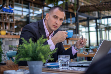 Businessman working on his laptop and writing in a notebook while sitting in a cafe