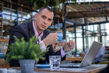 Businessman working on his laptop and writing in a notebook while sitting in a cafe