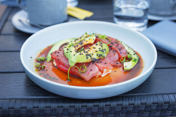 Fresh tuna fillet served with avocado, fresh tomato and sauce and garnished with black sesame seeds on wooden table. Healthy eating. Flexitarian diet.