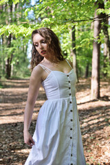 Fototapeta premium Pretty, young woman posing in the forest, wearing white dress. Green surroundings during spring in Poland.