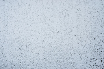 Closeup of rain drops on window on grey sky background