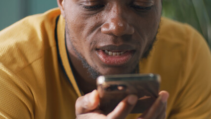 African American male in yellow t shirt talking and sending audio message on smartphone