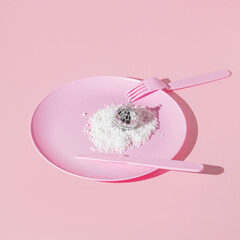 Christmas and New Year creative layout with pastel pink plate, fork, knife, snow and  disco ball christmas decoration on pastel pink background. 80s or 90s aesthetic fashion food restaurant concept.