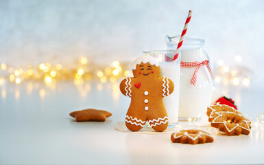 Close up traditional christmas milk in glass, jug with cookies on Christmas lights background. Festive food, Christmas celebration traditions