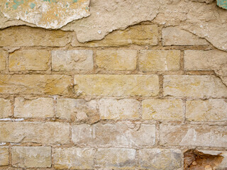 A beige brick wall from which a layer of paint has fallen off.