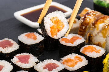 chinese chopsticks hold a roll with red fish on the background of the table with food