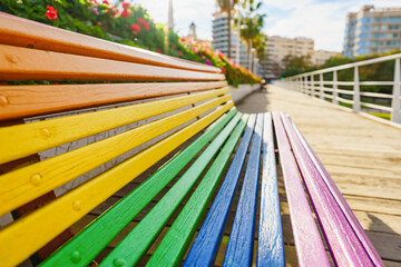 Bench painted with rainbow colours. Shallow depth of field. Blurry background.