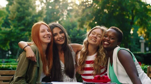 A friend group of four very attractive and independent women are sitting at a table posing and huddling together being very happy, cheerful while being outside