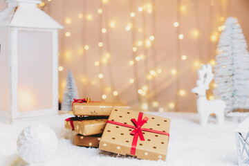 Christmas fairy tale composition with eco-friendly cardboard gift boxes on the snow with Christmas tree, deer, a festive lantern with warm lights bokeh background. Merry Xmas and Happy new year card.