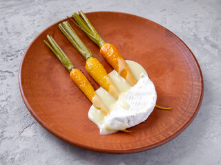 Side view of caramelized young carrots with hot soft cheese on a clay plate.
