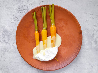 Top view of glazed baby carrots with hot camembert cheese.