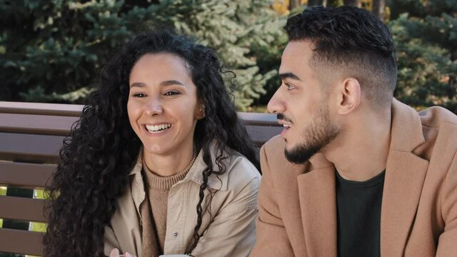 Attractive girl and handsome bearded man have fun communicate outdoors hispanic couple sit on bench in park young family smiling happily husband and wife enjoy pleasant conversation talking discussing