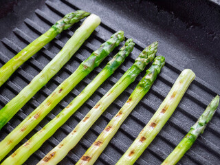 Side view of grilled green asparagus on a black frying pan.