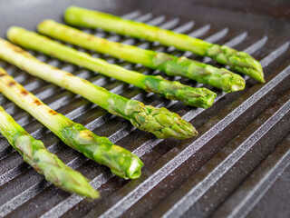 Top view of grilled green asparagus on a black frying pan.