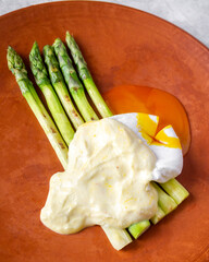 Side view of grilled asparagus, poached egg and parmesan coulis. The yolk flows onto the plate from the cut egg.