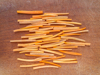 Top view of a wooden board with carrots cut into strips. Slicing technique julienne.