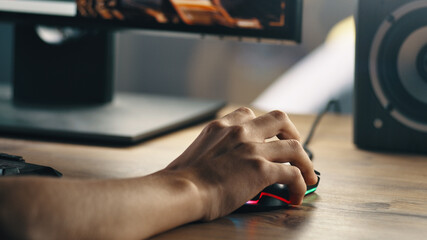 Unrecognizable teenager using computer mouse to aim weapon while sitting at desk and playing videogame at home