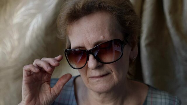 portrait of an elderly woman in dark glasses, then she takes them off