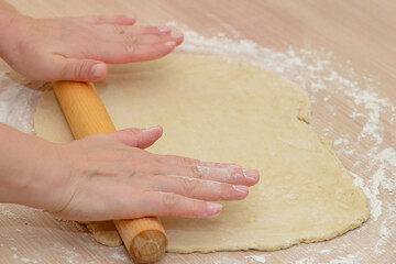 Women's hands roll out the dough on the table with a rolling pin