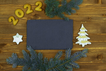 Christmas, New Year. Composition with numbers 2022, gingerbread cookies and chalkboard on wooden background, place for text