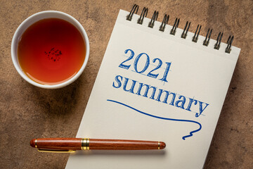 2021 summary - writing in a notebook with a cup of tea, end of year business concept