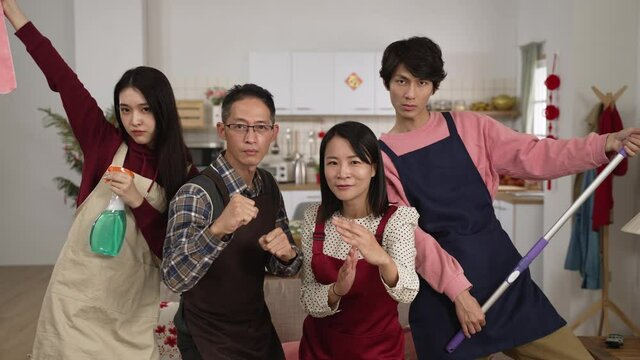 slow motion of funny asian family of four holding mop and sanitary spray and standing with kung fu gestures while looking at camera posing in a modern home interior. well prepared for spring cleaning