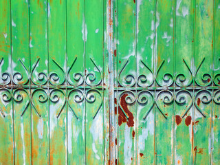 Part of a metallic green fence and gate. Colorful stains of paint and rust on the surface.