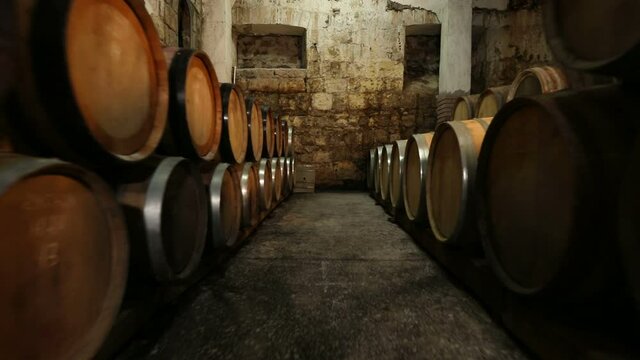 A Wine Cellar. Storage Room for Wine in Bottles and Barrels. Old wine in a dark underground vault. Wooden oak whiskey, wine, cognac, brandy or beer barrels. Bottles on wooden shelves.